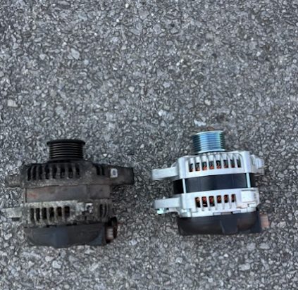 Old and new alternators side by side on the pavement, from a 2007 Toyota 4Runner